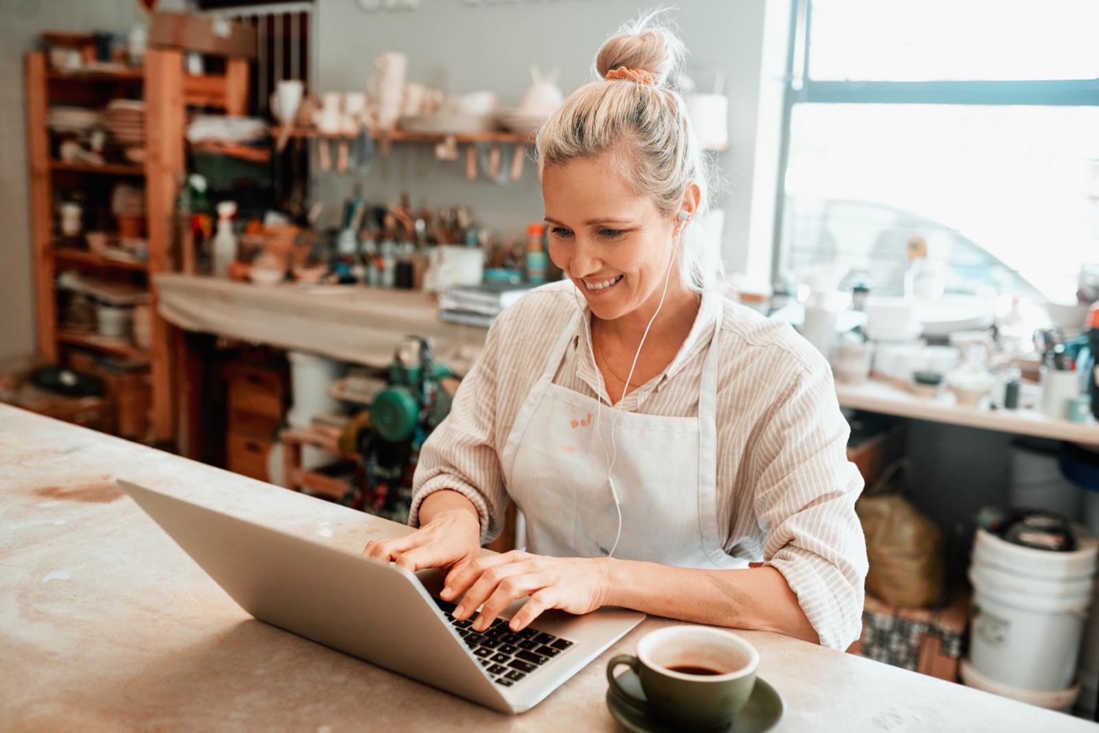 A woman using a laptop at a sunlit workshop counter