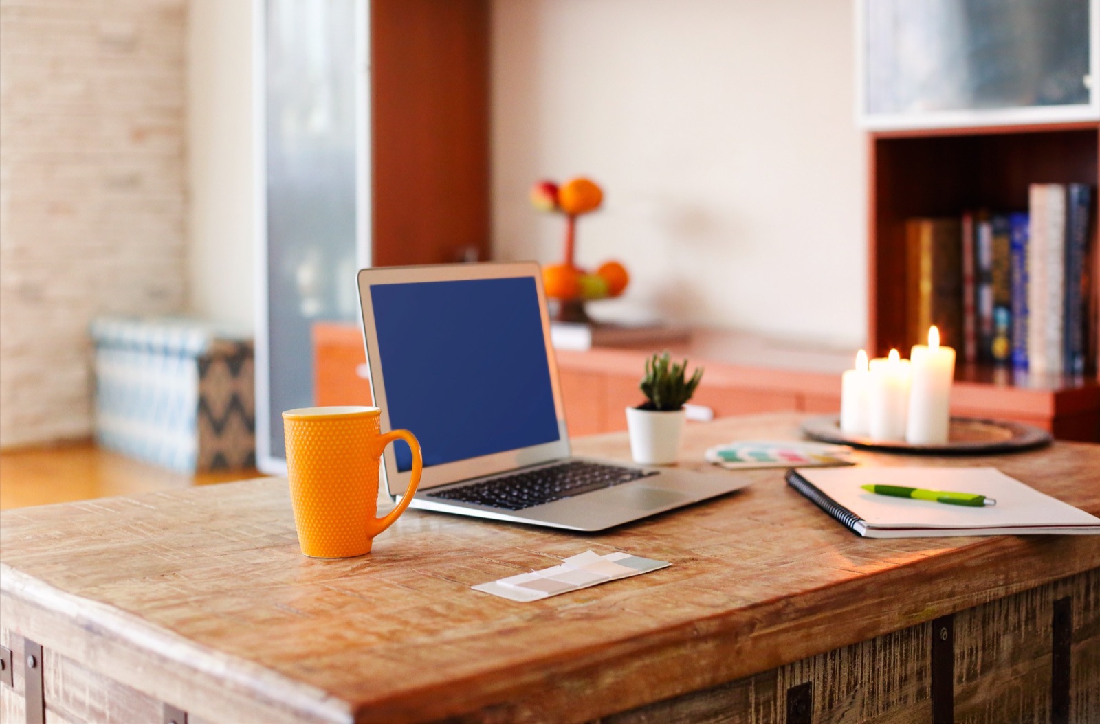 A laptop, notebook, and orange mug on a warm wooden desk